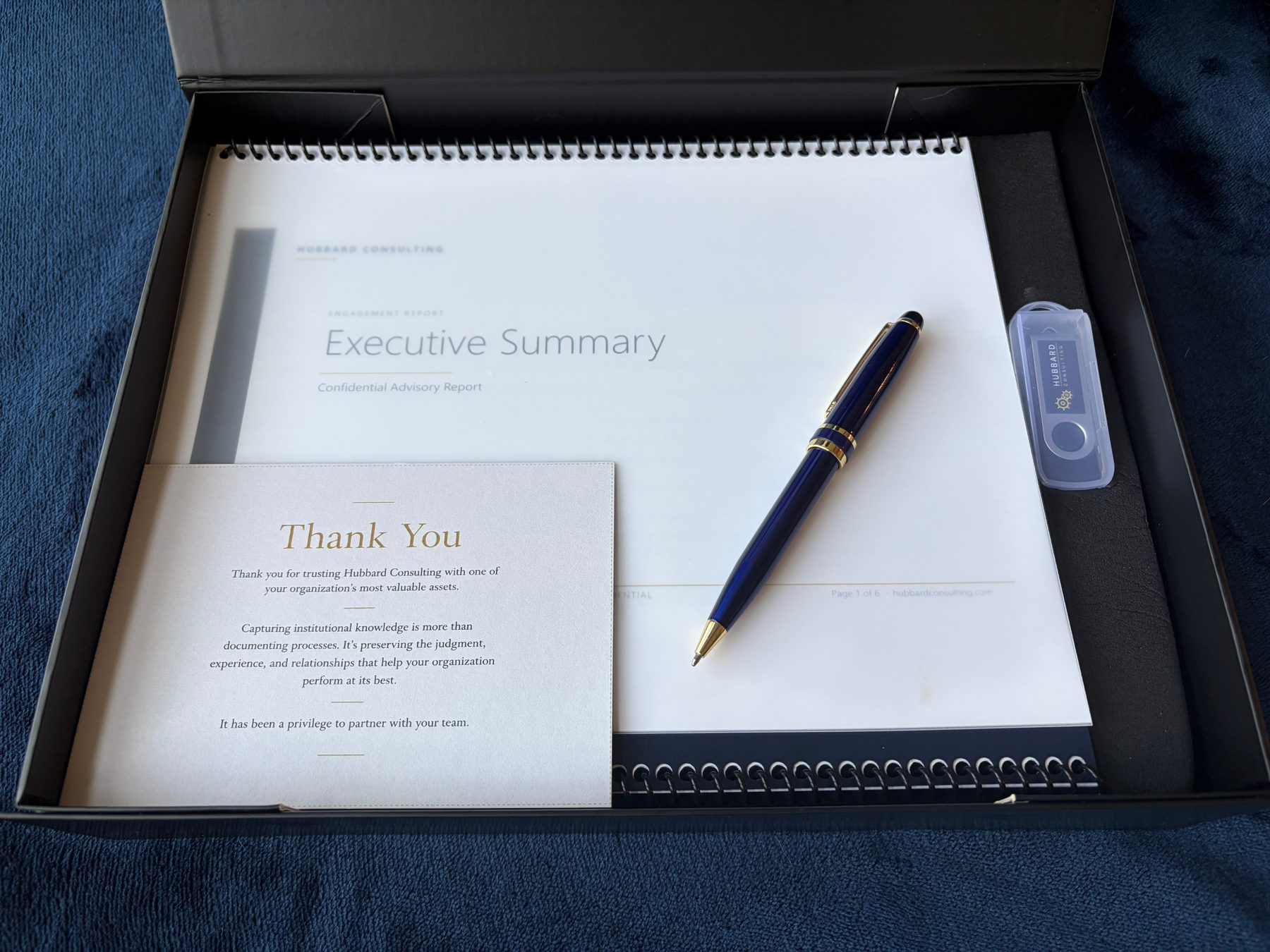 Open Hubbard Consulting client deliverable package showing the Executive Summary, spiral-bound Successor Acceleration Playbook, USB drive, pen, and thank-you card.